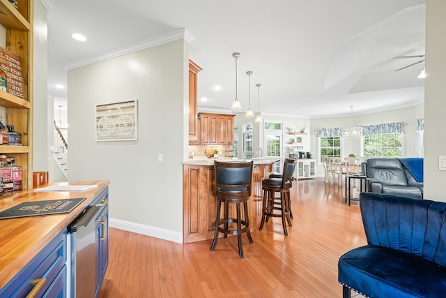 kitchen featuring decorative light fixtures, light hardwood / wood-style floors, crown molding, and a breakfast bar