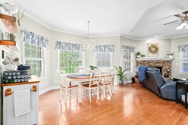 dining room featuring ornamental molding, light hardwood / wood-style flooring, ceiling fan with notable chandelier, and a fireplace