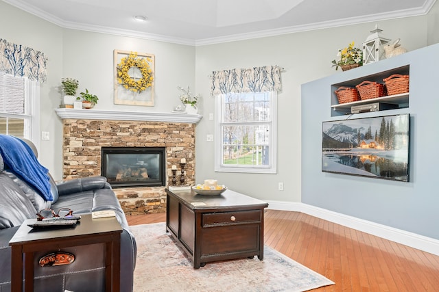 living room with light hardwood / wood-style flooring, ornamental molding, and a stone fireplace