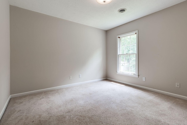 carpeted empty room featuring baseboards, visible vents, and a textured ceiling