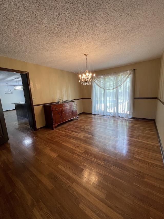 unfurnished dining area with dark hardwood / wood-style flooring, a textured ceiling, and a notable chandelier