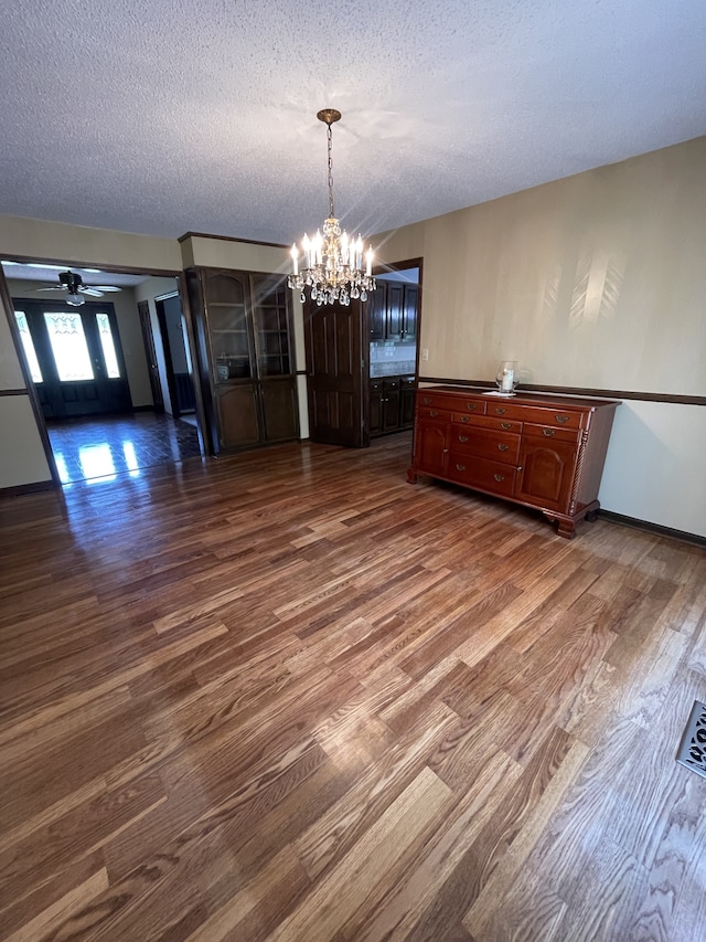 unfurnished dining area with ceiling fan with notable chandelier, a textured ceiling, and dark wood-type flooring