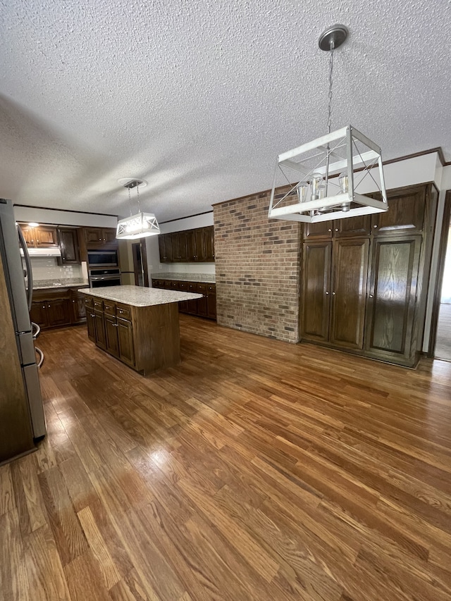 kitchen featuring hanging light fixtures, appliances with stainless steel finishes, dark brown cabinets, a kitchen island, and dark hardwood / wood-style flooring