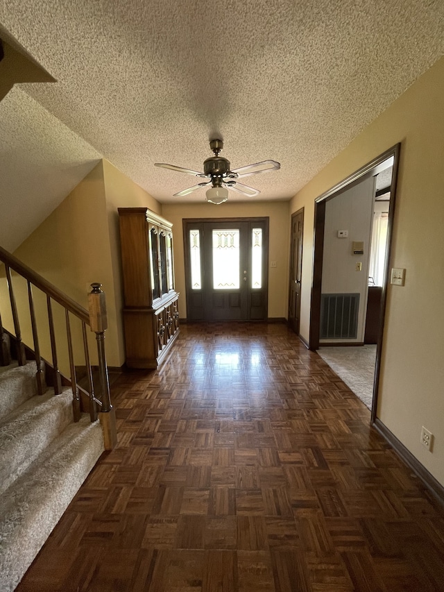 foyer featuring dark parquet flooring, ceiling fan, and a textured ceiling