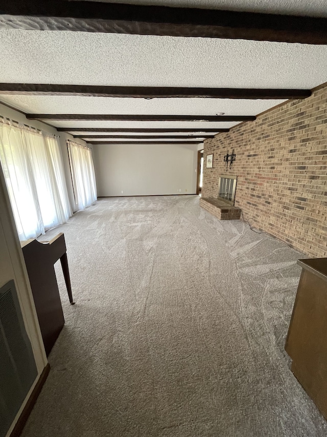 unfurnished living room with carpet flooring, beamed ceiling, brick wall, and a brick fireplace