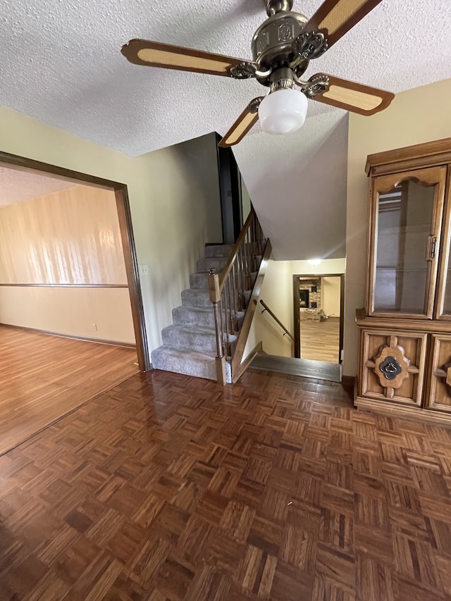 staircase featuring ceiling fan, parquet floors, a textured ceiling, and vaulted ceiling