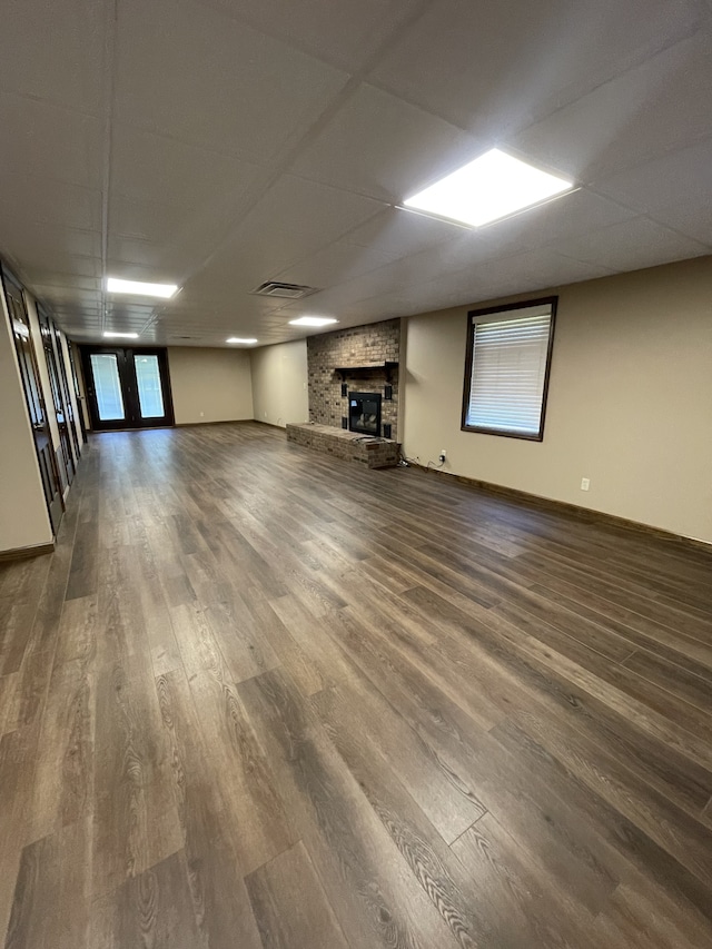 basement with a paneled ceiling, wood-type flooring, and a brick fireplace