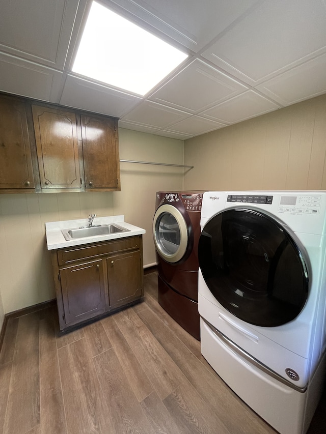 laundry room with washer and clothes dryer, cabinets, wood-type flooring, and sink