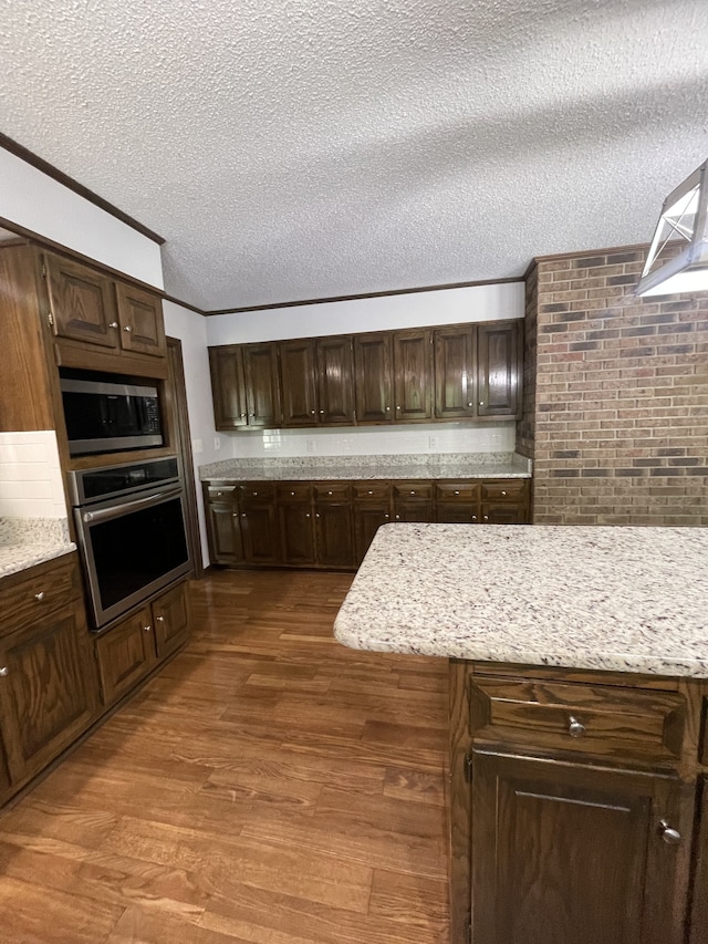 kitchen with stainless steel appliances, light stone counters, dark hardwood / wood-style flooring, a textured ceiling, and dark brown cabinets