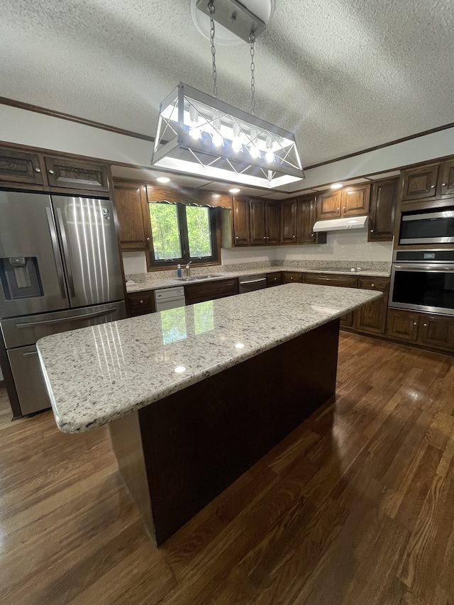 kitchen with a textured ceiling, a kitchen island, decorative light fixtures, and appliances with stainless steel finishes