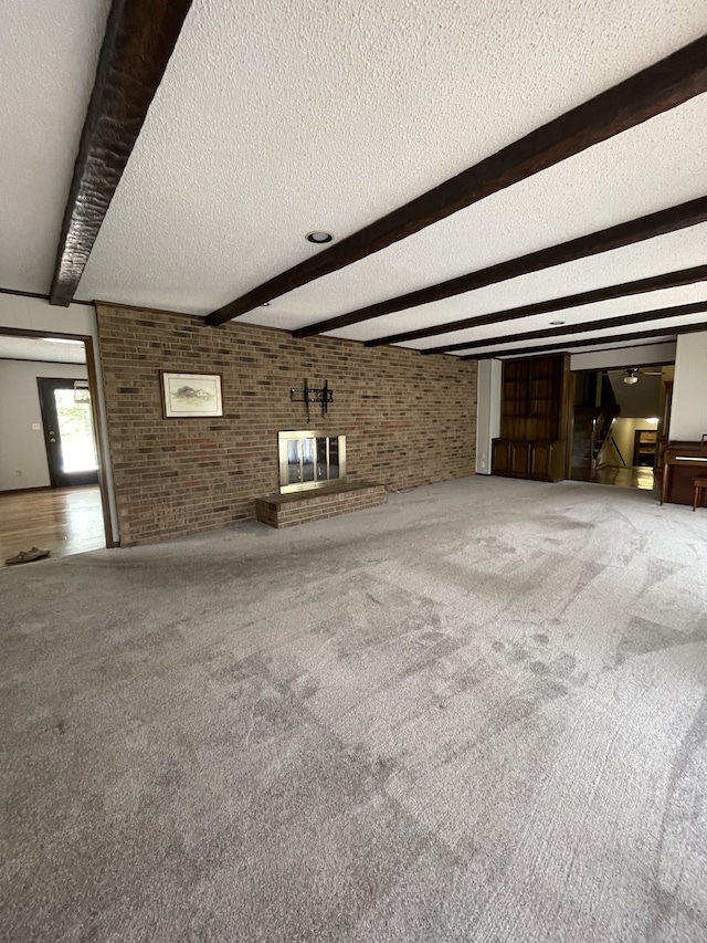 unfurnished living room with beam ceiling, carpet floors, a textured ceiling, and brick wall