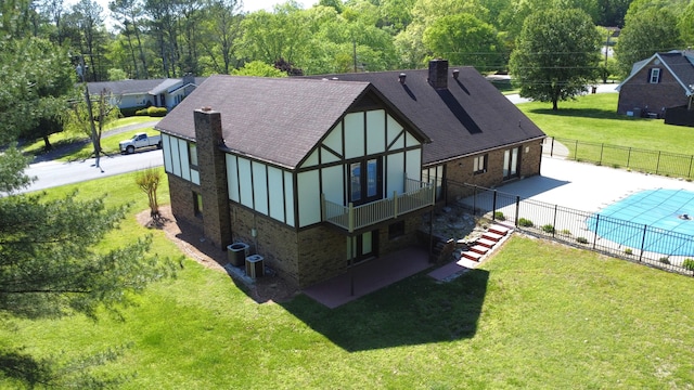 back of house with central AC, a covered pool, a patio area, and a lawn