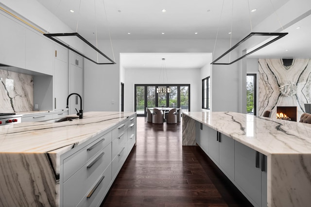 kitchen with decorative light fixtures, a fireplace, a large island with sink, white cabinetry, and dark hardwood / wood-style floors