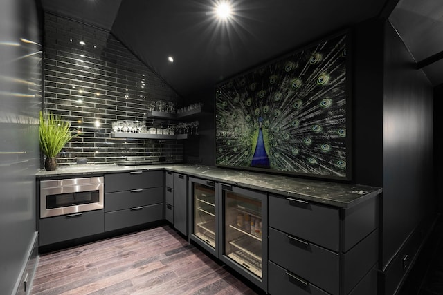 kitchen with gray cabinetry, wall oven, tasteful backsplash, dark stone countertops, and hardwood / wood-style floors