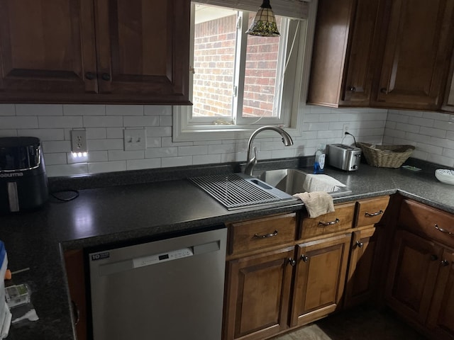 kitchen with stainless steel dishwasher, dark countertops, decorative backsplash, and a sink