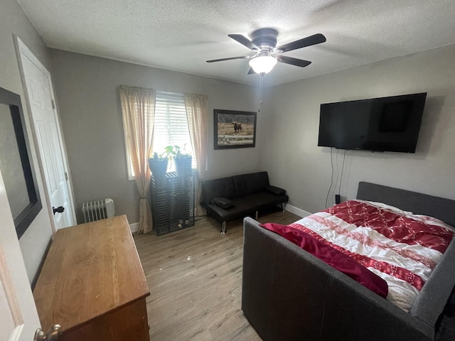 bedroom featuring light wood finished floors, radiator, baseboards, a textured ceiling, and a ceiling fan