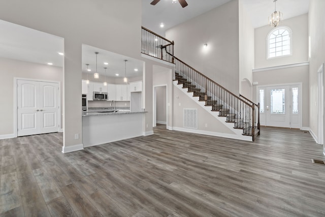 unfurnished living room with sink, ceiling fan with notable chandelier, hardwood / wood-style flooring, and a towering ceiling