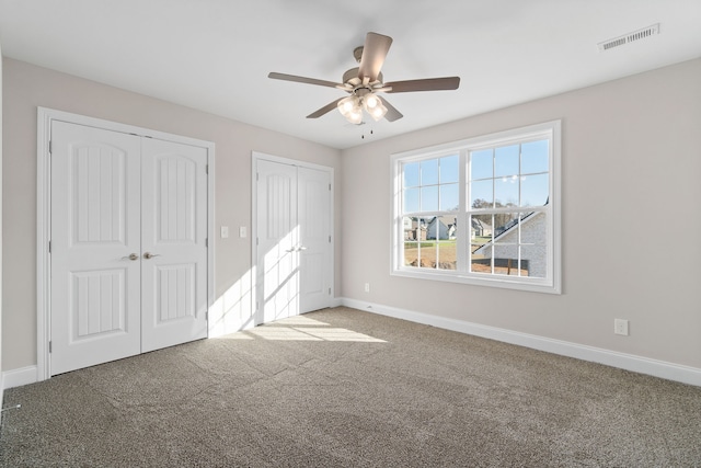 unfurnished bedroom featuring ceiling fan, carpet floors, and two closets