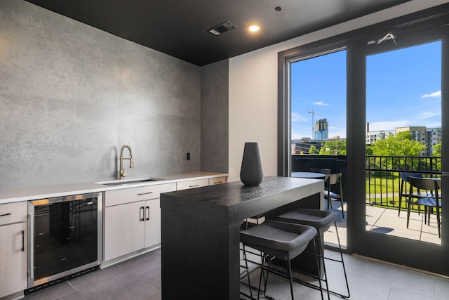 bar with sink, tile floors, white cabinetry, and beverage cooler