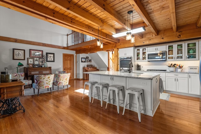 kitchen with decorative light fixtures, light hardwood / wood-style floors, an island with sink, and white cabinetry