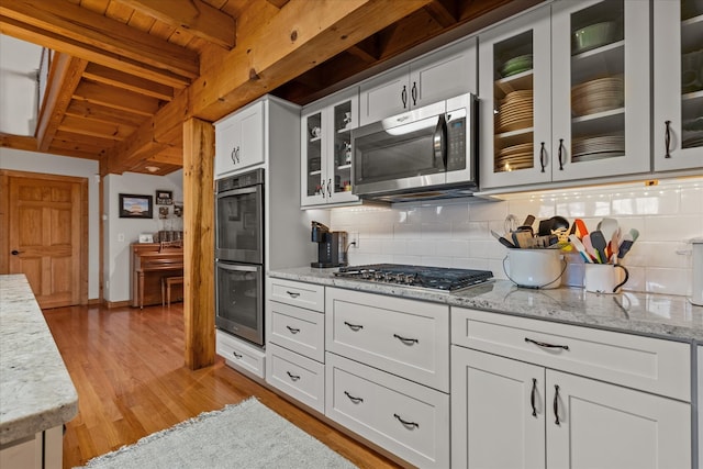 kitchen with beam ceiling, stainless steel appliances, light wood-type flooring, and tasteful backsplash