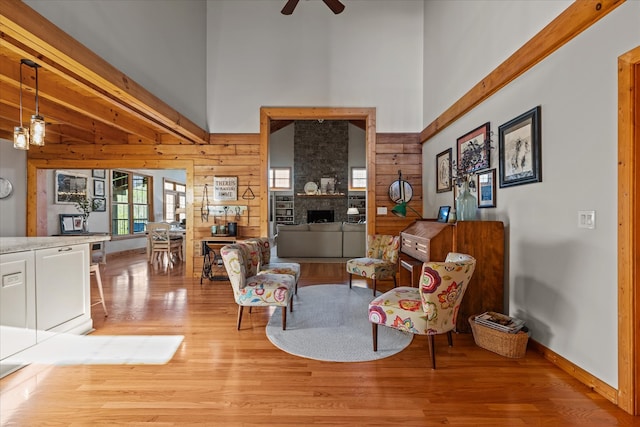 sitting room featuring wooden walls, light wood-type flooring, a high ceiling, beam ceiling, and ceiling fan