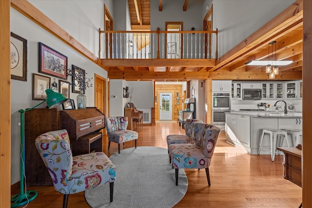 living room with sink, light hardwood / wood-style floors, beamed ceiling, and a high ceiling