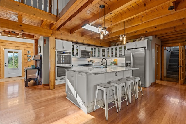 kitchen with decorative light fixtures, light hardwood / wood-style flooring, appliances with stainless steel finishes, a center island with sink, and sink