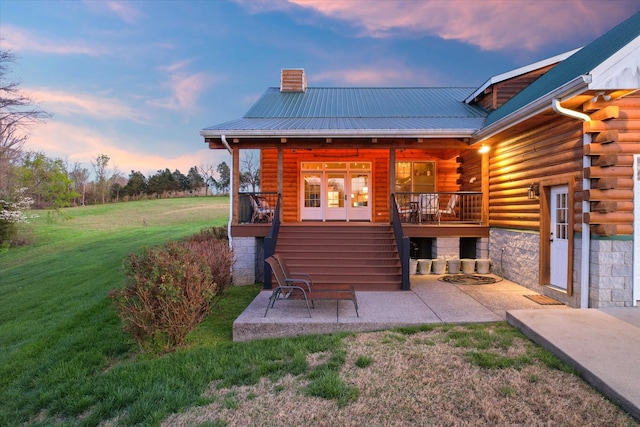 back house at dusk featuring french doors, a patio, and a lawn