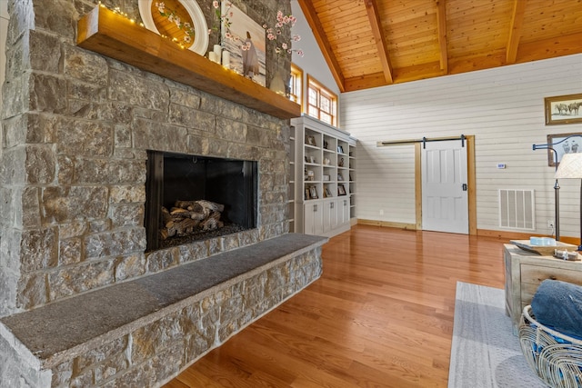 living room featuring a stone fireplace, a barn door, lofted ceiling with beams, hardwood / wood-style flooring, and wooden ceiling