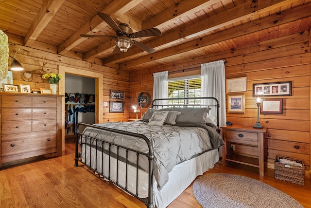 bedroom featuring light hardwood / wood-style floors, wood ceiling, beam ceiling, a spacious closet, and wood walls