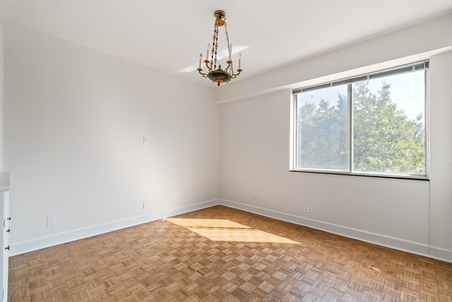 spare room featuring parquet flooring and an inviting chandelier