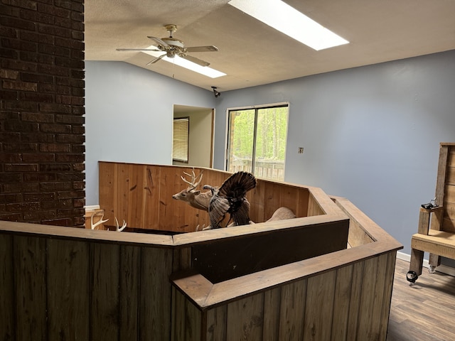 interior space with hardwood / wood-style flooring, ceiling fan, lofted ceiling with skylight, and brick wall