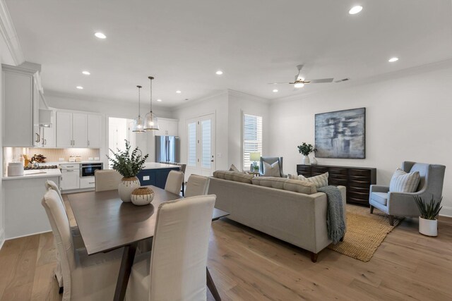 dining room with ceiling fan with notable chandelier, ornamental molding, and light hardwood / wood-style flooring