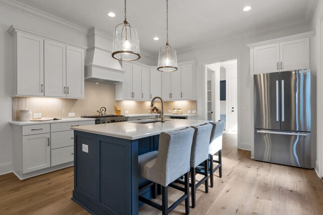 kitchen featuring custom exhaust hood, sink, an island with sink, appliances with stainless steel finishes, and light hardwood / wood-style floors