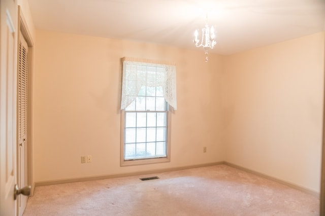 carpeted empty room with an inviting chandelier