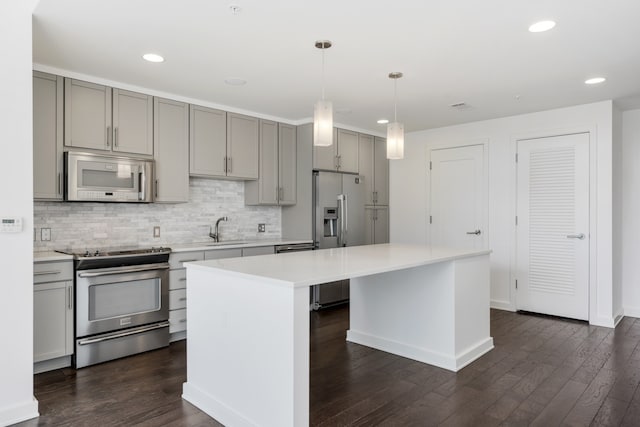 kitchen with a kitchen island, sink, dark wood-type flooring, hanging light fixtures, and stainless steel appliances