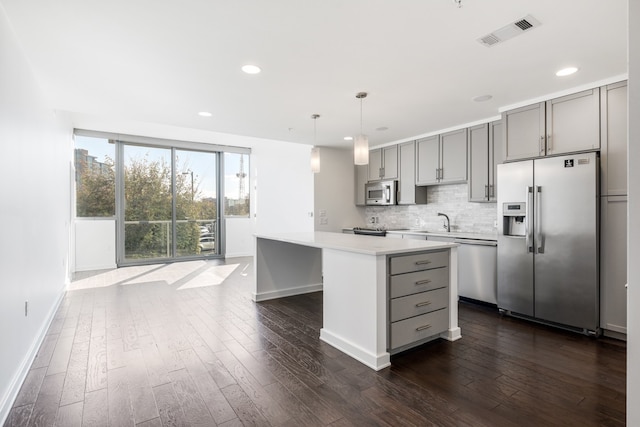 kitchen with decorative light fixtures, a kitchen island, gray cabinets, stainless steel appliances, and dark hardwood / wood-style floors