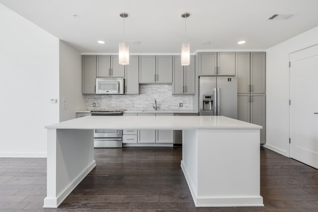 kitchen with a center island, pendant lighting, dark hardwood / wood-style flooring, appliances with stainless steel finishes, and tasteful backsplash