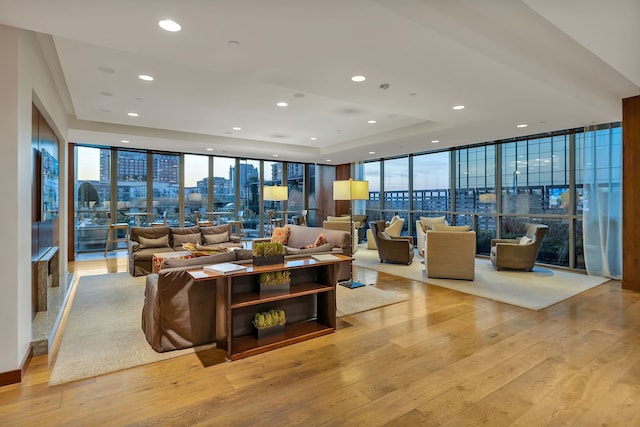 living room with floor to ceiling windows, light wood-type flooring, and a tray ceiling