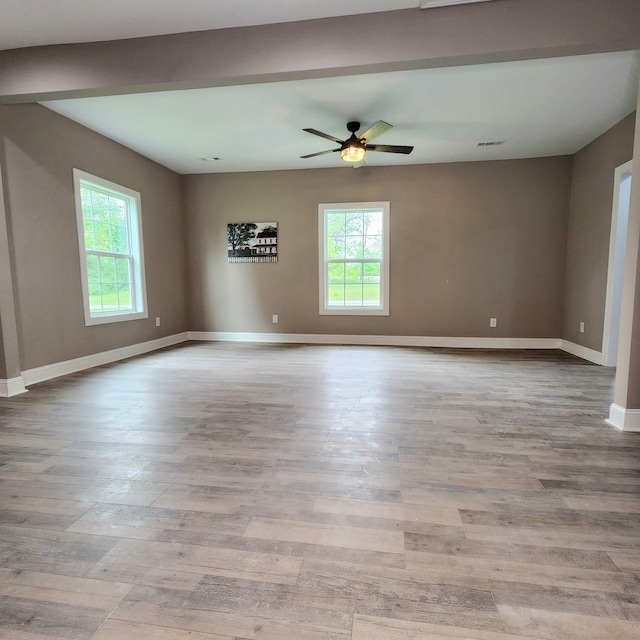 empty room with a wealth of natural light, wood-type flooring, and ceiling fan