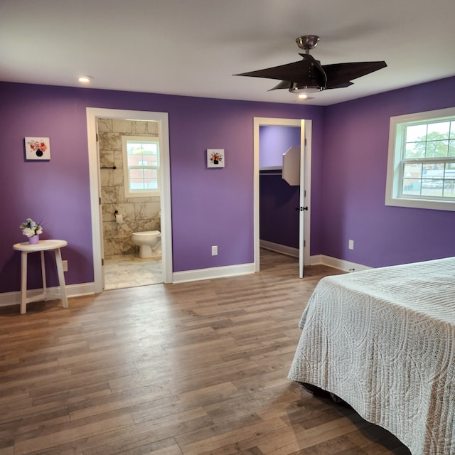 bedroom featuring ceiling fan, hardwood / wood-style flooring, ensuite bathroom, and multiple windows