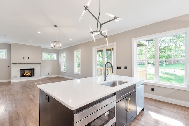 kitchen featuring a premium fireplace, sink, light wood-type flooring, hanging light fixtures, and an island with sink