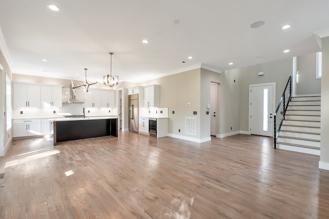 kitchen featuring white cabinetry, decorative light fixtures, built in fridge, light hardwood / wood-style flooring, and a kitchen island with sink