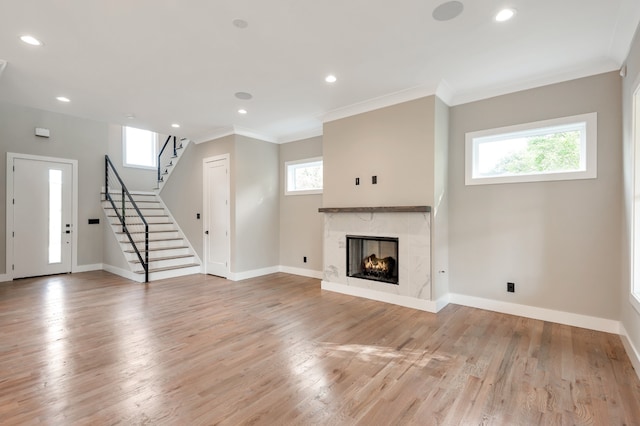 unfurnished living room featuring a wealth of natural light, hardwood / wood-style floors, crown molding, and a premium fireplace