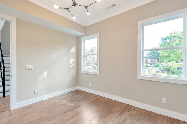 spare room with plenty of natural light, light hardwood / wood-style flooring, and a notable chandelier