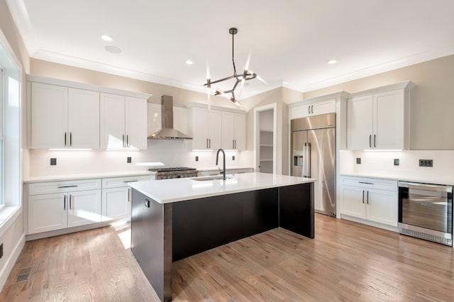 kitchen featuring wall chimney exhaust hood, light wood-type flooring, beverage cooler, white cabinetry, and built in fridge