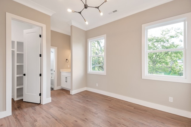 unfurnished bedroom with a notable chandelier, light hardwood / wood-style flooring, crown molding, and ensuite bathroom