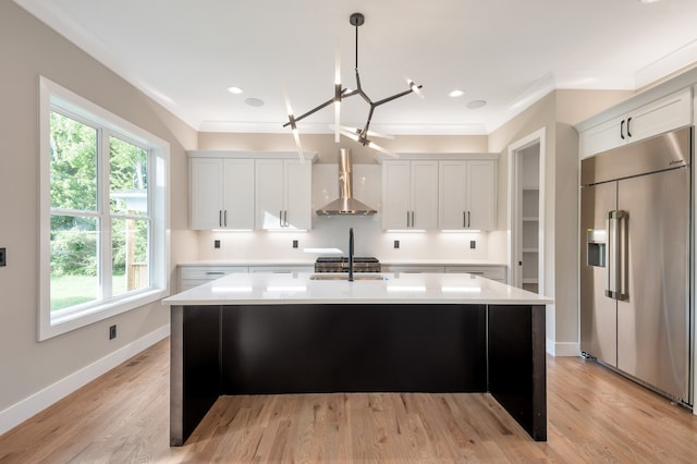 kitchen featuring plenty of natural light, stainless steel built in fridge, light hardwood / wood-style floors, and wall chimney exhaust hood