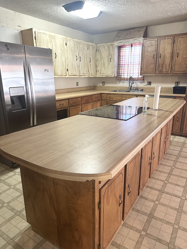 kitchen featuring stainless steel fridge, a kitchen island, a textured ceiling, black electric stovetop, and sink